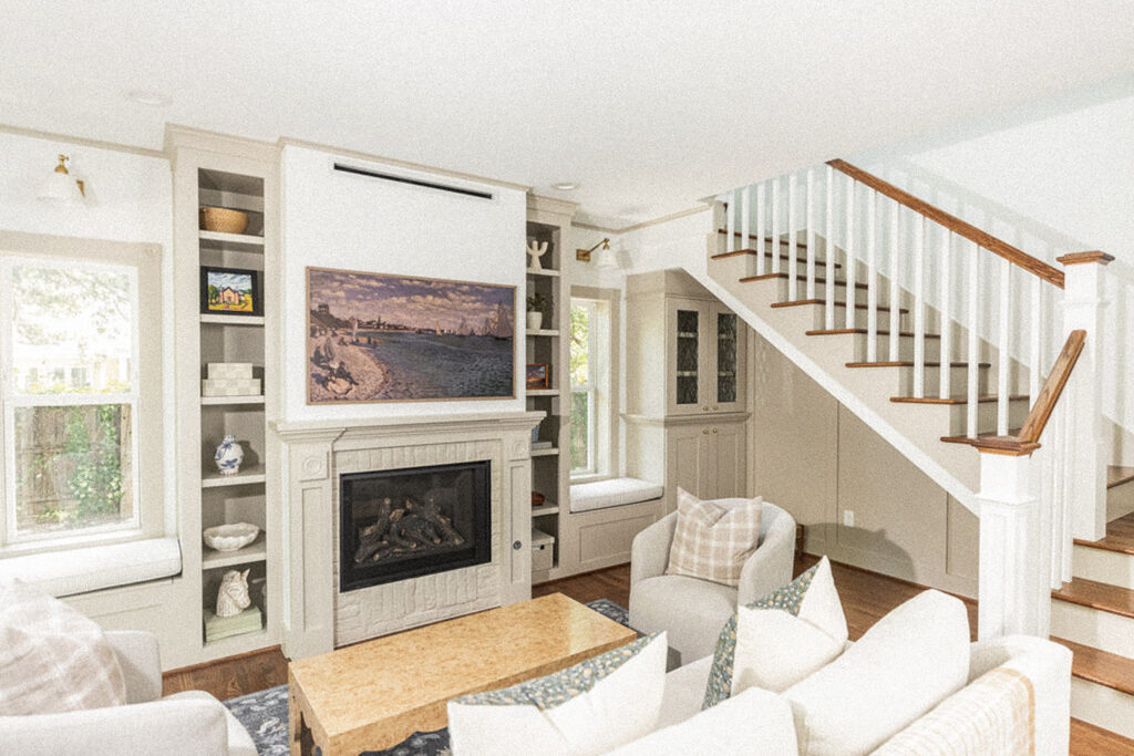 Cozy living room with built ins surrounding a fireplace. TV above the fireplace and a book nook under the stairway.